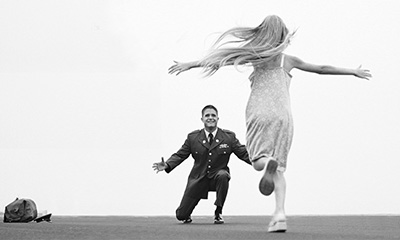 Young girl running across a tarmac to meet her father, dressed in a uniform on bended knee.