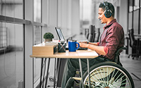 Man in a wheelchair working on a laptop while wearing headphones
