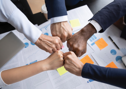 Five hands meeting together in the center of a table - Monster Government Solutions CHCO Roundtable