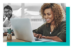 Woman working on a laptop, a man smiling in the background.