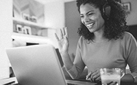 Woman wearing a headset and waving at a laptop screen.