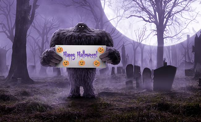 Monster in a spooky graveyard holding a Happy Halloween sign with pumpkins on it.