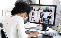 Woman in front of a computer in a remote meeting smiling and writing